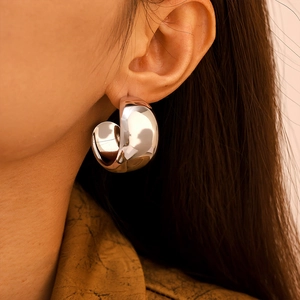 Polished silver stainless steel C-shaped hoop earrings worn on a model's ear