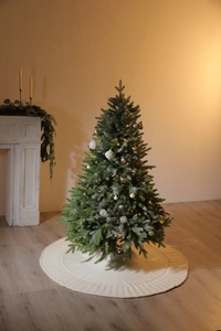 Close-up of white knitted Christmas tree skirt with festive holiday decor and warm LED lights