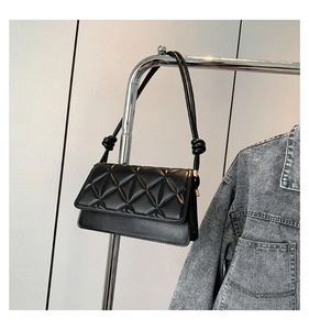 Detail of black quilted leather shoulder bag with decorative knotted strap and metal hardware