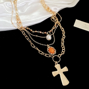 Macro detail of layered gold necklace with white pearl, orange gem and cross pendant