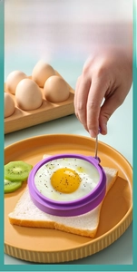 Macro shot of purple silicone fried egg mold with handle on toast with colorful plates