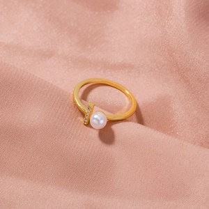 Detail of a gold open ring featuring a white pearl and zircons on pink silk fabric