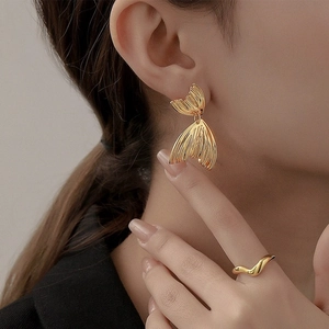 Détail de boucles d'oreilles queue de poisson dorées et bague ondulée sur modèle