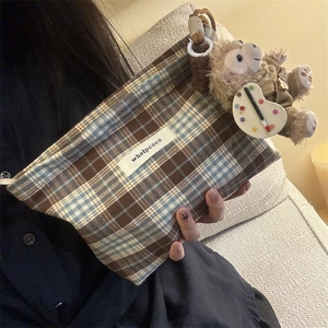 Portable brown and blue plaid pouch with a plush charm and brand label on fabric