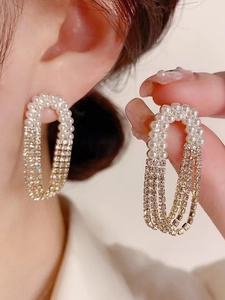 Detail of elegant gold earrings with white pearls and shimmering rhinestone tassels