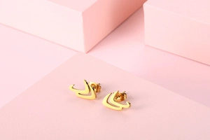 Detail of geometric gold stud earrings displayed on pink minimalist props with soft lighting