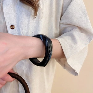 Close-up of a chunky black acrylic geometric resin bangle on a woman's wrist