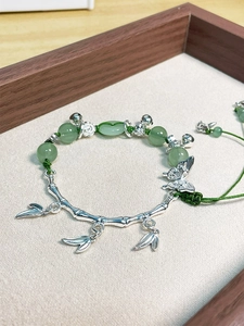 Detail of bamboo joint bracelet with green jade beads and butterfly charms in a tray