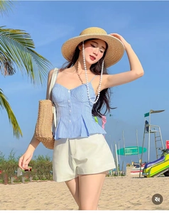 Outdoor shot of a blue striped camisole top paired with high-waist shorts and straw hat