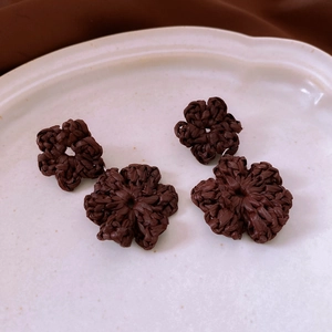 Detail of bohemian dark brown hand-woven raffia flower earrings in a white ceramic dish