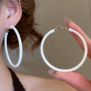 Macro shot of large white leather-wrapped circular earrings with spiral texture and gold hooks