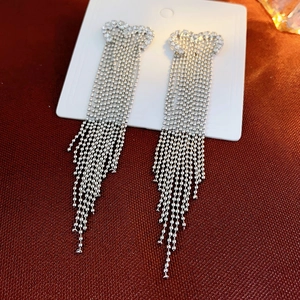 Macro detail of long silver fringe earrings with rhinestone heart studs on a display card