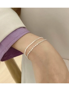 Detail eines silbernen S925-Sterlingsilber-Doppelarmbands mit funkelnden Perlen am Handgelenk