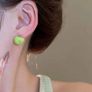 Close-up of a green apple enamel stud earring with a gold star accent on a model's ear