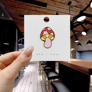 Detailed close-up of a red and pink cartoon mushroom enamel pin held on a white card