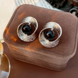 Detail of twisted silver hoop earring with black bead on a luxury brown velvet box