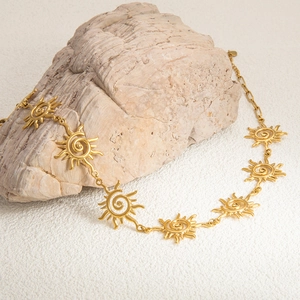 Detailed view of golden sun-patterned stainless steel necklace on a textured stone base