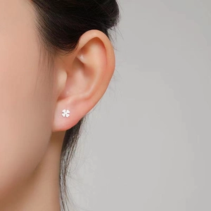 Close-up of minimalist silver clover stud earring worn on ear showing delicate detail