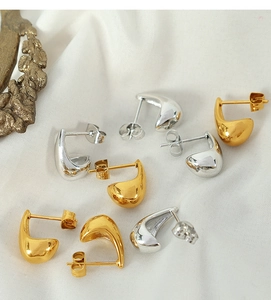 Detailed view of polished gold and silver water drop earrings on white silk fabric