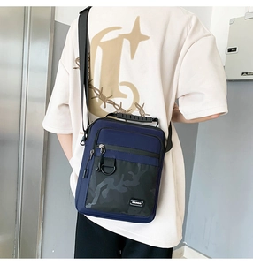 Detail view of a navy blue crossbody bag with camouflage pocket and a black D-ring hook