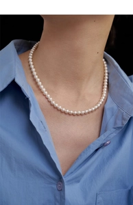 Close-up of a French vintage single-layer pearl necklace worn with a blue shirt