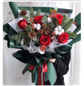 Close-up of Christmas bouquet with red roses, pine cones, and festive green wrapping paper