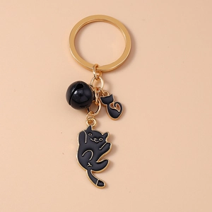 Detail of a black cartoon cat keychain with small silhouette charm and golden hardware