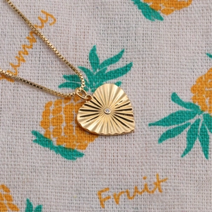 Détail du pendentif cœur doré avec texture rayonnante et petite pierre étincelante
