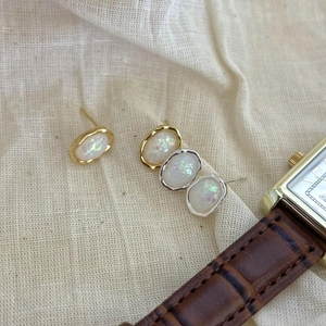 Macro detail of oval opal stud earrings in gold and silver plating on linen fabric