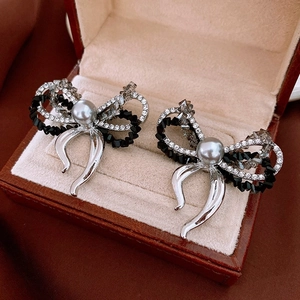 Macro shot of silver bow earrings with black crystals and grey faux pearls in a box