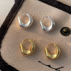 Close-up of sleek gold and silver U-shaped hoop earrings on beige fabric background