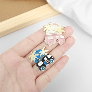 Enamel beach camper badges with palm trees and golden outlines held in hand