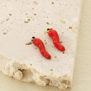 Detail of red enamel chili charms in gold and silver finish on a stone texture