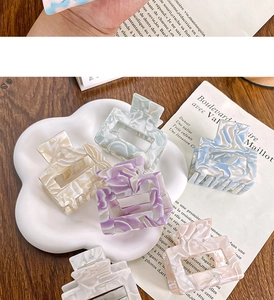 Macro display of diverse acetate claw clips in pastel marble textures on a wooden tray
