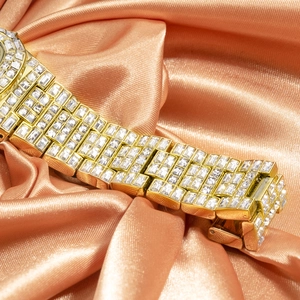 Close-up of luxury gold watch band with rectangular crystals on peach satin background