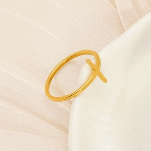 Detail of minimalist gold cross ring placed on a ceramic dish with silk background