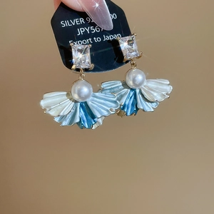 Detailed close-up of fan-shaped pearl earrings with zircon and silver needle on display card