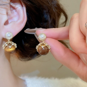 Detailed view of 18K gold plated pearl and tiger eye earrings worn on model's ear