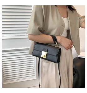 Detail of black leather crossbody bag with golden metal twist lock shown on a model