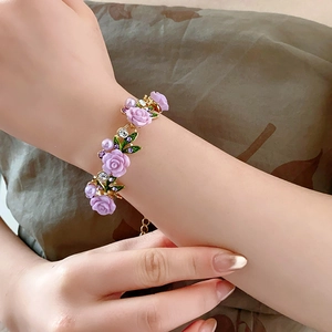 Gros plan du bracelet doré avec fleurs violettes et perles porté au poignet du mannequin