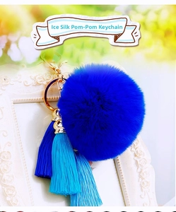 Macro view of blue ice silk tassels and plush fur pom-pom with a golden metal keychain