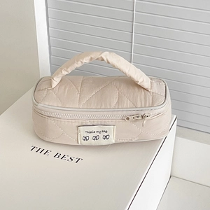 Detailed quilted texture and black label on a creamy beige nylon vanity bag