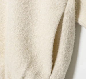 Detailed close-up of pocket stitching on soft off-white sherpa fleece jacket texture