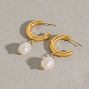 Detalle de pendientes de aro en C de acero de titanio dorado con perlas barrocas blancas