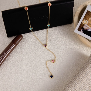 Détail d'un collier en Y doré orné de pierres en forme de cœur sur un fond texturé beige