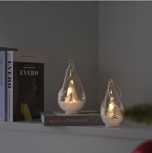 Detail of two light-up glass teardrop ornaments with warm LED lights and snowy mini trees