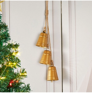 Three vintage gold metal Christmas bells with rustic hemp rope hanging on a wall
