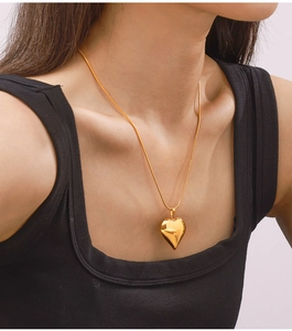 Close-up of a polished gold heart pendant on a delicate snake chain worn by a model