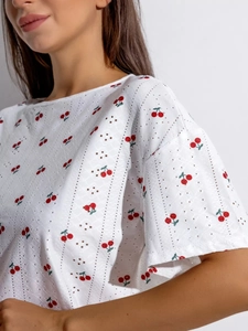 Detail der Eyelet-Stickerei mit rotem Kirschdruck auf weißem Kurzarm-Oberteil
