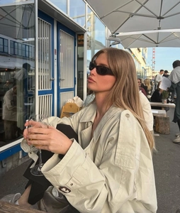 Close-up of black narrow frame sports sunglasses worn with a beige trench coat outdoors